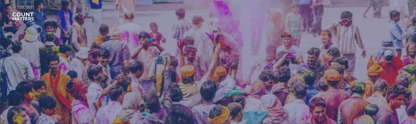 Farverig menneskemængde fejrer Holi-festivalen med folk, der kaster pulver op i luften. Ideel til at illustrere crowd analytics, overvågning af eventdeltagelse og sikkerhedsstyring i realtid med CountMatters, logo i hjørnet.