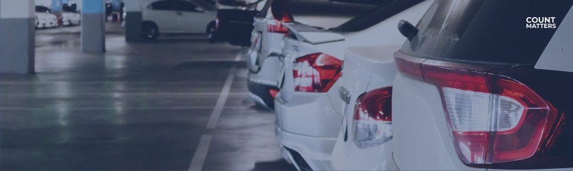 Række af parkerede biler i et indendørs parkeringshus. Ideel til at illustrere analyser af parkeringsbelægning, måling af besøgsflow og overvågning af kapacitet i realtid med CountMatters, logo i hjørnet.
