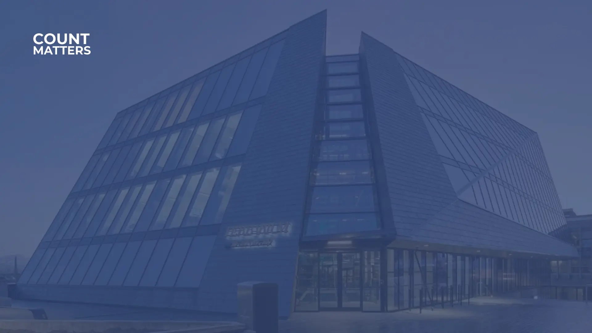 Modernes Glasgebäude mit kantiger Architektur in der Abenddämmerung, das zur Veranschaulichung der intelligenten Gebäudeanalyse und Besucherüberwachung mit CountMatters dient.